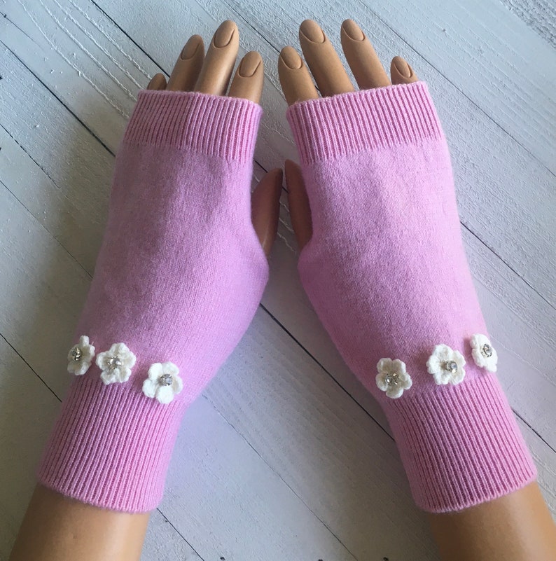 May include: A pair of pink fingerless gloves with white crocheted flowers on the cuffs.