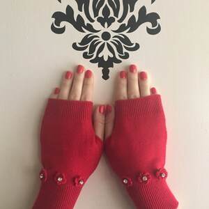 May include: Red fingerless gloves with a crocheted flower detail on the cuff. Each flower has a rhinestone in the center.