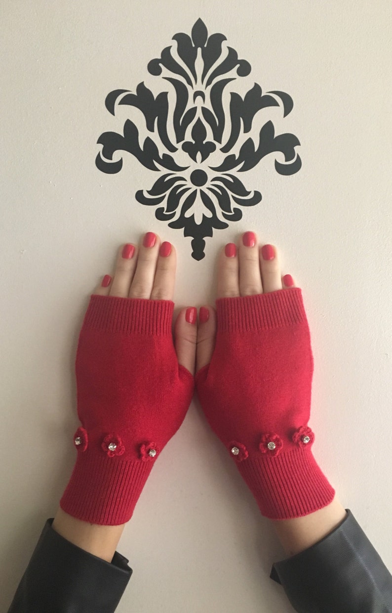 May include: Red fingerless gloves with a crocheted flower detail on the cuff. Each flower has a rhinestone in the center.