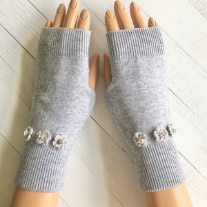 May include: Gray fingerless gloves with a row of small white crocheted flowers with rhinestones on the cuff.