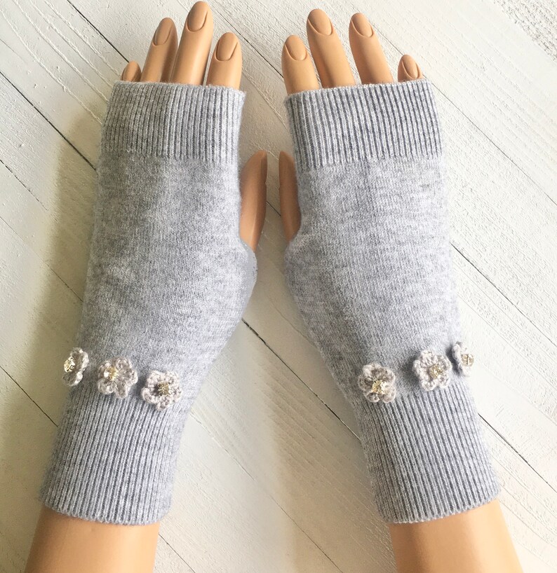 May include: Gray fingerless gloves with a row of small white crocheted flowers with rhinestones on the cuff.