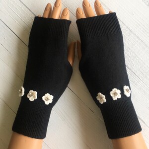 May include: Black fingerless gloves with white crocheted flowers embellished with rhinestones.