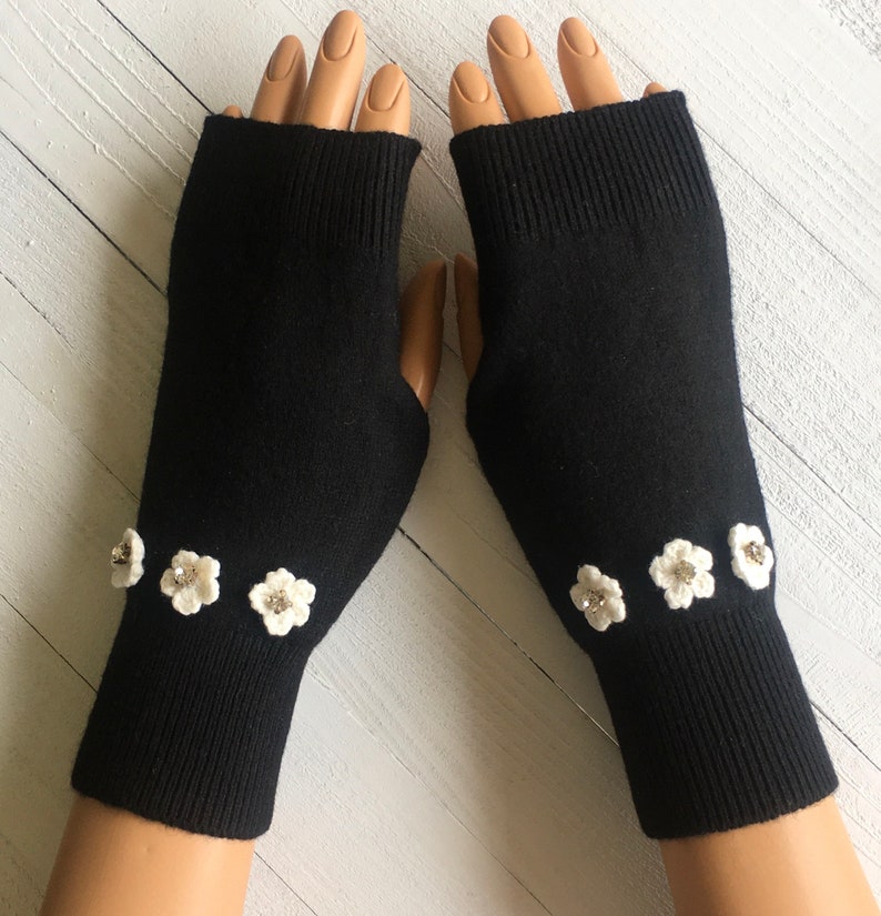 May include: Black fingerless gloves with white crocheted flowers embellished with rhinestones.