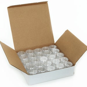May include: A cardboard box with the lid open, revealing a full set of 36 clear plastic containers. The containers are arranged in a grid pattern inside the box.