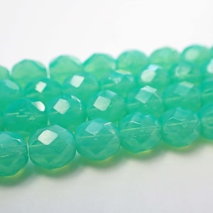 May include: Close-up of a strand of faceted, light green beads. The beads are round with multiple flat surfaces, creating a sparkling effect. The beads are strung together, suggesting their use in jewelry making or crafts.