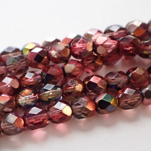 May include: Close-up of strands of faceted beads in shades of burgundy and iridescent hues. The beads have a multi-faceted design, reflecting light and creating a shimmering effect. The beads are strung together, suggesting their use in jewelry making or crafting.