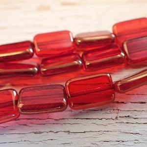 May include: Close-up of rectangular red glass beads. The beads are translucent with a slight golden hue around the edges. The beads are strung together, showcasing their shape and colour.