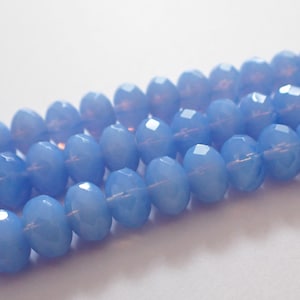 May include: Close-up of light blue faceted oval beads strung together. The beads have a glossy finish and are arranged in parallel rows, creating a textured surface. The beads are a soft, pastel blue color.