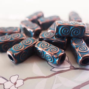 May include: A collection of rectangular beads with a teal and copper finish. Each bead features a spiral design on the surface. The beads are scattered, showcasing their detailed craftsmanship and color variations. Ideal for jewelry making.