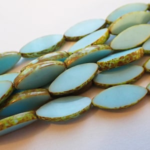 May include: Close-up of a strand of oval-shaped beads. The beads have a light blue center with a brown and yellow mottled edge. The beads are strung together, creating a textured and colorful pattern.