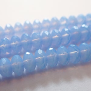 May include: Close-up of several strands of light blue faceted beads. The beads have a translucent quality and are strung together, creating a delicate and shimmering effect. The beads are a soft, pastel blue color.