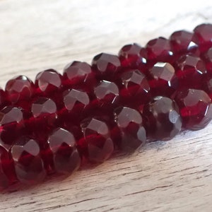 May include: Close-up of a strand of faceted, deep red beads. The beads have a multi-faceted design, catching the light and creating a sparkling effect. The beads are strung together, suggesting they are for jewelry making or crafting.