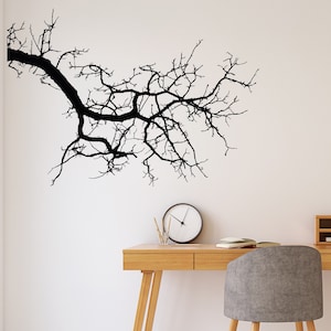 May include: A black silhouette of a bare tree branch on a white wall, with a wooden desk and a gray chair in front of it.