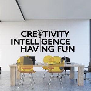 May include: A modern office with a white wall featuring the text "CREATIVITY IS INTELLIGENCE HAVING FUN" with a lightbulb graphic. The office has a wooden table with four yellow chairs and a black office chair.