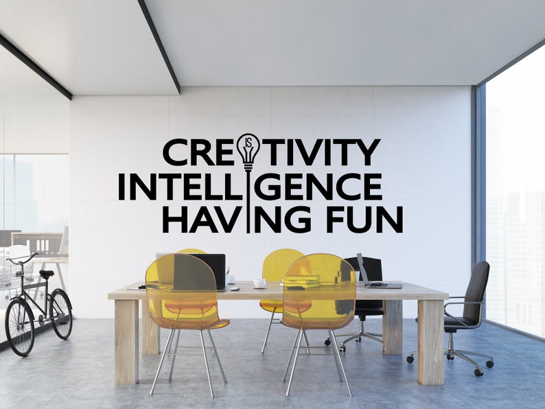 May include: A modern office with a white wall featuring the text "CREATIVITY IS INTELLIGENCE HAVING FUN" with a lightbulb graphic. The office has a wooden table with four yellow chairs and a black office chair.