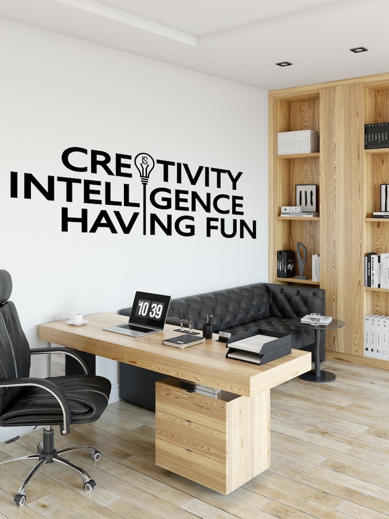 May include: A home office with a wooden desk, black leather chair, and a black leather sofa. The wall has a black and white motivational quote that reads "Creativity is intelligence having fun".