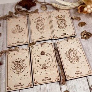 May include: Seven wooden ornaments with a star design and a tarot card image on each. The cards are "The High Priestess", "The Empress", "The Emperor", "The Magician", "The Chariot", "The Tower", and "The Star".