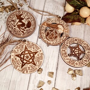 May include: Four wooden ornaments with a witch, pentagram, and solstice themes. The ornaments are decorated with intricate designs and text, including "Merry Witchmas" and "We will survive the darkness".