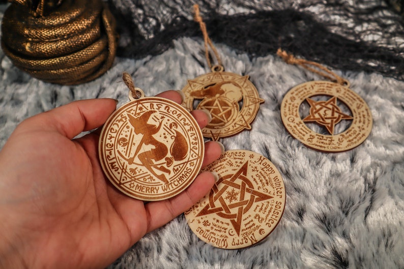 May include: Four wooden ornaments with intricate designs, including a witch flying on a broomstick, a pentagram, and a snowflake. The ornaments are all circular and have a rustic, hand-crafted look.