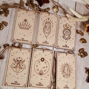 May include: Seven wooden cards with gold foil accents and illustrations of tarot cards. The cards are labeled with the names of the tarot cards: The High Priestess, The Empress, The Emperor, The Magician, The Chariot, The Tower.