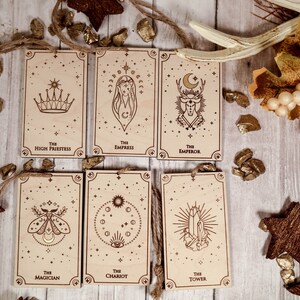 May include: Six wooden tarot cards with gold accents and a star-filled background. The cards feature the following titles: The High Priestess, The Empress, The Emperor, The Magician, The Chariot, and The Tower.