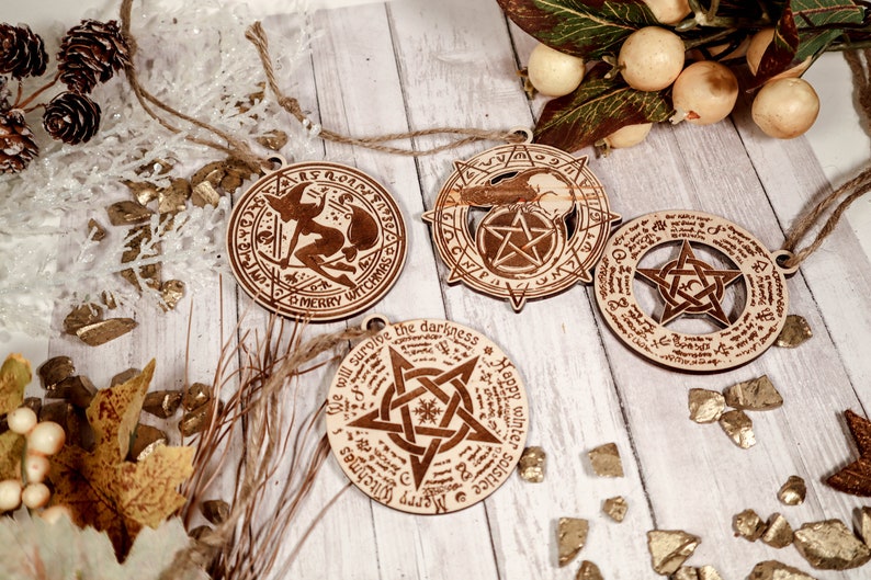 May include: Four wooden ornaments with a witch, a pentagram, and a phrase about surviving the darkness. The ornaments are hanging from a twine string and are on a white wooden background with gold glitter.