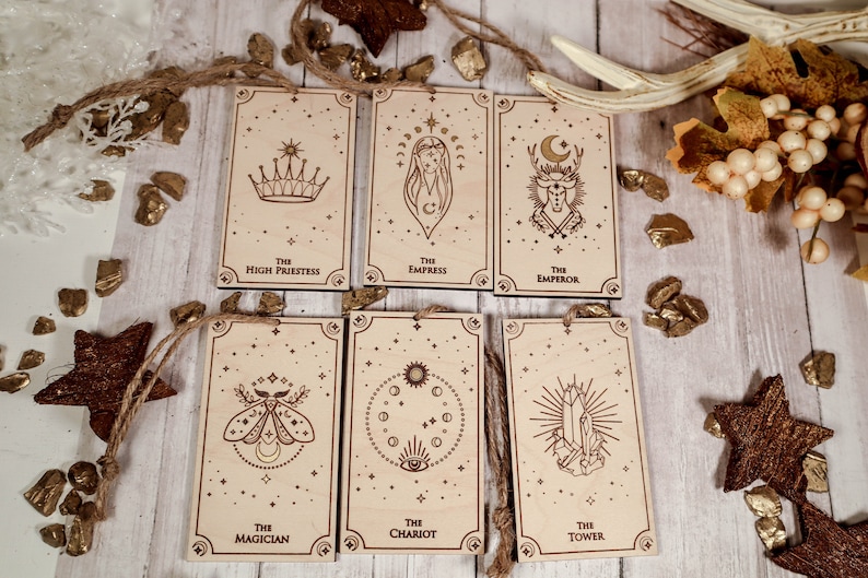 May include: Set of seven wooden tarot cards with gold foil accents. The cards feature illustrations of the High Priestess, Empress, Emperor, Magician, Chariot, Tower, and a moth. Each card has a star-studded background.
