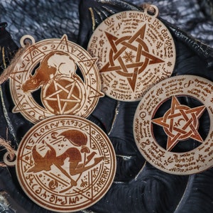 May include: Three wooden ornaments with pentagram designs and inscribed text. The text includes "Merry Witchmas", "We will survive the darkness", and "Solstice".
