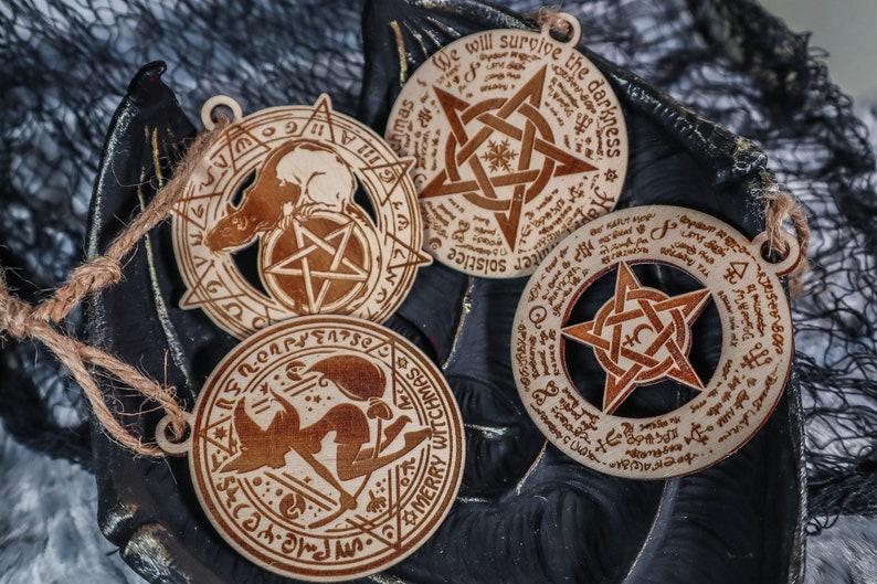 May include: Three wooden ornaments with pentagram designs and inscribed text. The text includes "Merry Witchmas", "We will survive the darkness", and "Solstice".