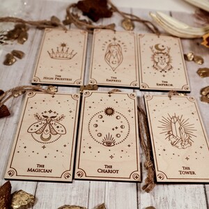 May include: Six wooden ornaments with a star and moon theme. Each ornament features a different tarot card image, including The Magician, The Chariot, The Tower, The High Priestess, The Empress, and The Emperor.