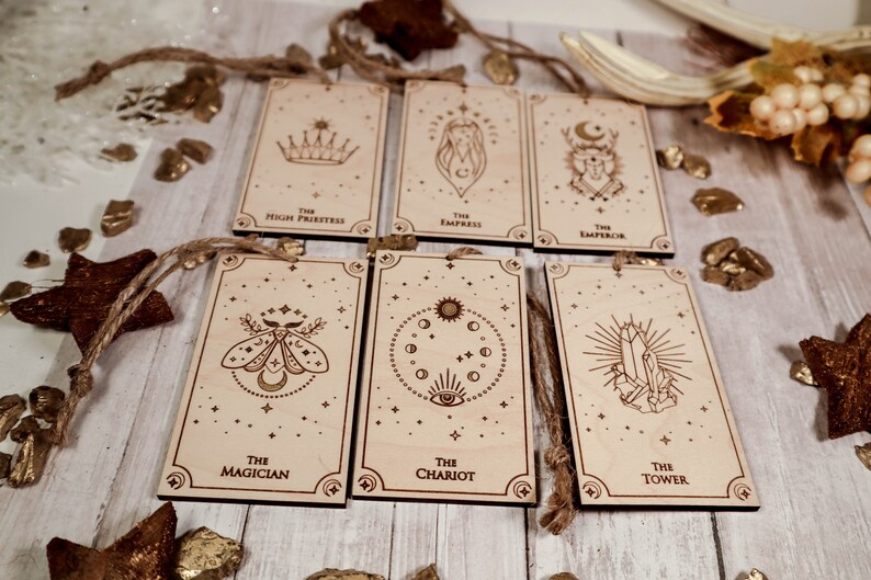 May include: Six wooden ornaments with a star and moon theme. Each ornament features a different tarot card image, including The Magician, The Chariot, The Tower, The High Priestess, The Empress, and The Emperor.
