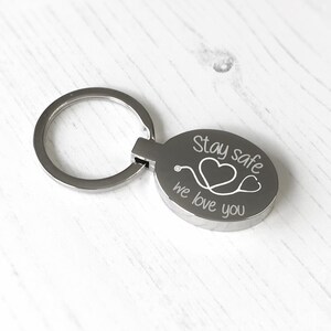 May include: Silver keychain with an oval charm that says "Stay safe we love you" with a stethoscope and two hearts engraved on it.