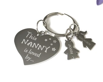 Pode incluir: Chaveiro de coração prateado com o texto "This NANNY is loved by..." e dois pequenos pingentes prateados com os nomes "JOSH" e "IMOGEN" gravados.