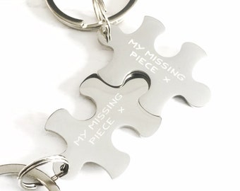 Op de afbeelding: Een zilveren sleutelhanger met twee in elkaar grijpende puzzelstukken. Elk stuk heeft de tekst "My Missing Piece" gegraveerd.