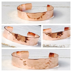 May include: A hammered copper bracelet with a wide, flat band. The bracelet is made of a single piece of copper that has been hammered to create a textured surface.