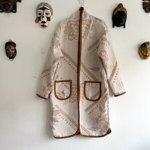 May include: A white quilted jacket with a brown floral pattern and brown trim. The jacket has two patch pockets on the front and a brown zipper closure.