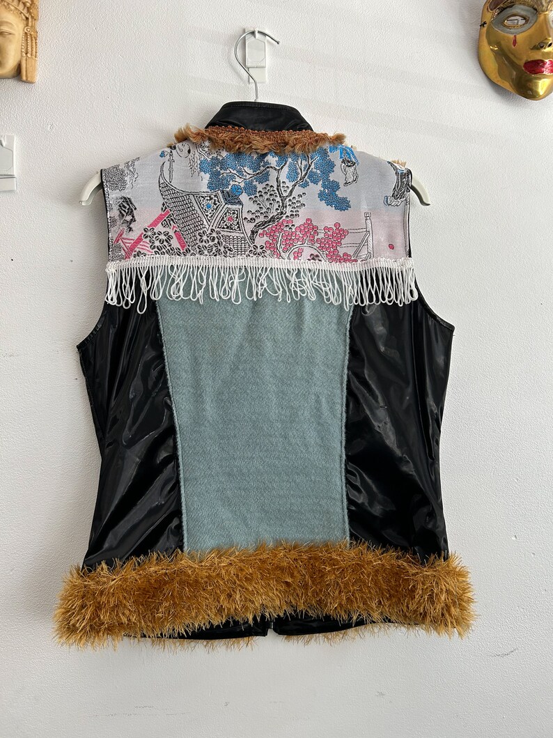 May include: A black sleeveless vest with a blue and white patterned fabric panel on the back. The vest has a brown fur collar and trim around the bottom.