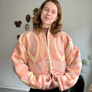 Puede incluir: Una chaqueta corta de color rosa y crema con un diseño estampado. La chaqueta tiene un diseño geométrico con fondo crema y detalles en rosa.