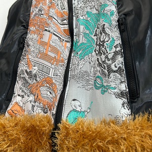 May include: Black puffer vest with a zipper closure and a brown faux fur trim. The vest features a colorful Asian-inspired print on the front.