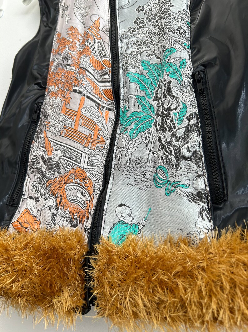 May include: Black puffer vest with a zipper closure and a brown faux fur trim. The vest features a colorful Asian-inspired print on the front.