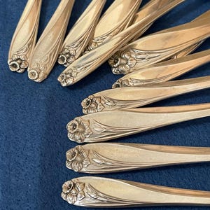 May include: Close-up of a collection of silver spoons. Each spoon features a floral design at the handle's end. The spoons are arranged on a blue surface, showcasing their intricate details and reflective surfaces.