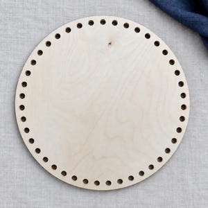 May include: A circular light-colored wooden base featuring a smooth, flat surface with a series of evenly spaced, small circular holes punched along the entire outer perimeter, designed for crafting or basket weaving projects.