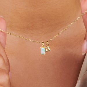 May include: A gold chain necklace with two charms: a small rectangular opal charm and a letter 'a' charm.