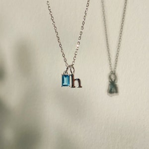 K&ouml;nnte beinhalten: Eine silberne Halskette mit einem blauen Edelstein und einem silbernen Anh&auml;nger mit dem Buchstaben 'h'.