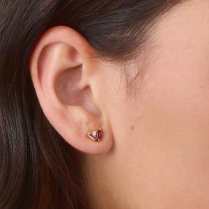 May include: A pair of gold stud earrings with a pink and white gemstone design.