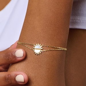 May include: A gold chain bracelet with a sun charm featuring a white mother-of-pearl inlay.