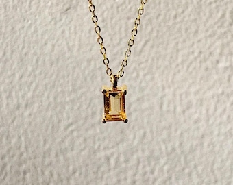 Könnte beinhalten: Eine goldene Kettenkette mit einem kleinen, rechteckigen Anhänger mit einem hellgelben Edelstein.