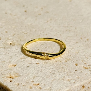 May include: A gold band ring with a single diamond accent. The ring is curved and has a simple design.