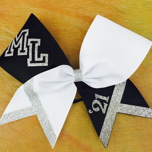 May include: Black and white cheer bow with silver glitter accents. The bow has the letters "ML" on one side and the number "'21" on the other side.