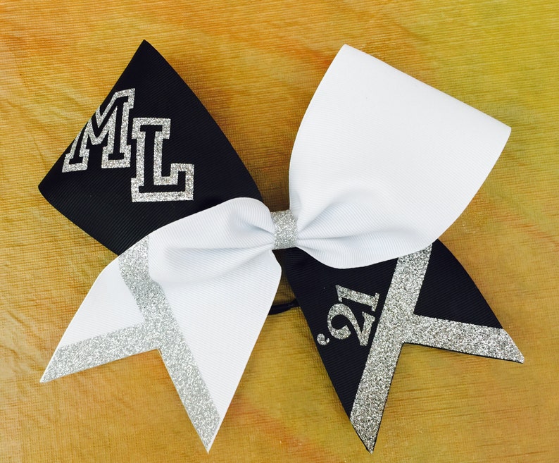 May include: Black and white cheer bow with silver glitter accents. The bow has the letters "ML" on one side and the number "'21" on the other side.